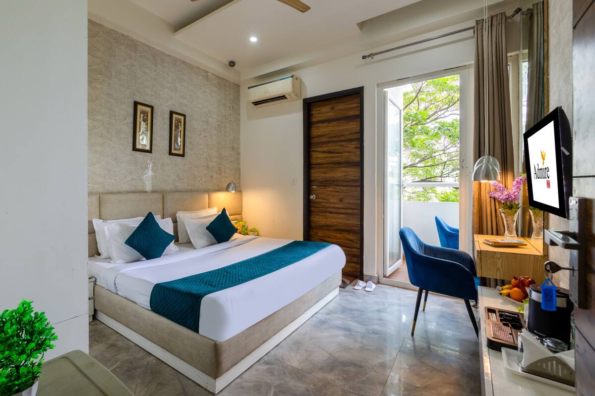 A modern hotel room with a large bed, a desk with a computer, a TV, and a view of the outdoors.