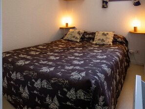 A bed with a dark patterned bedspread, two bedside lamps, and a wall-mounted picture.