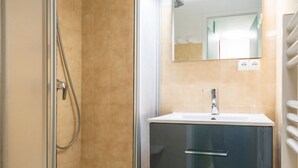 A bathroom with a glass shower enclosure, a sink with a mirror above it, and a towel rack on the right.