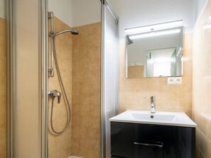 Een badkamer met een douche in een glazen cabine, een witte wastafel en een spiegel erboven.