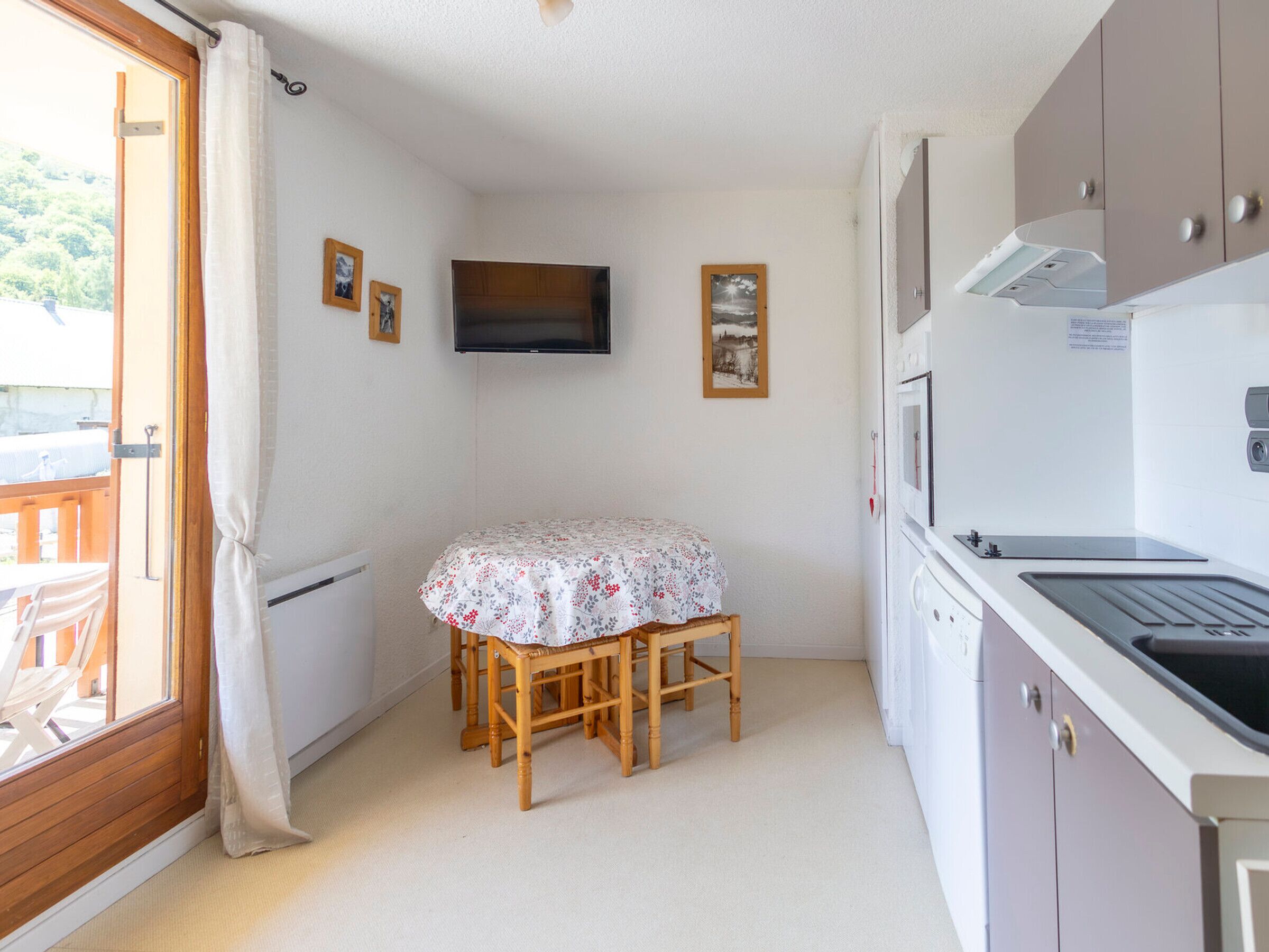 A compact kitchen with a dining table, wooden chairs, a television, and a built-in oven.