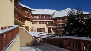 Ein mehrstöckiges Gebäude mit Balkonen, verschneitem Gelände und blauem Himmel.
