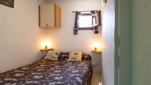 A small, cozy bedroom with a bed, two bedside lamps, a window with curtains, and a wall-mounted cabinet.