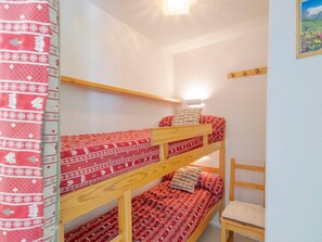 A bunk bed room with a wooden frame, a single bed with patterned bedding, and a chair.