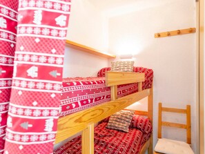 Een stapelbed met een rood beddegoed met patroon en kussens, een houten hoofdbord en een wandlamp.