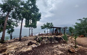 A wooden gazebo overlooking a rocky landscape with trees and a view of the sea. - Bukit Shoka Top View Camp (Giricahyo)