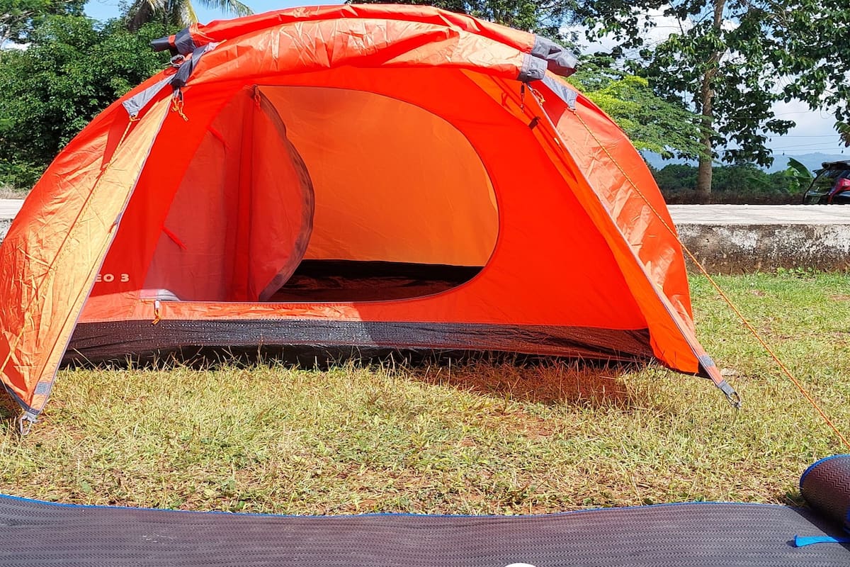 Tenda vermelha montada na grama com um tapete azul à frente.