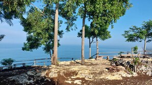 A rocky terrain with trees and a wooden fence overlooking a body of water. - Bukit Shoka Top View Camp (Giricahyo)
