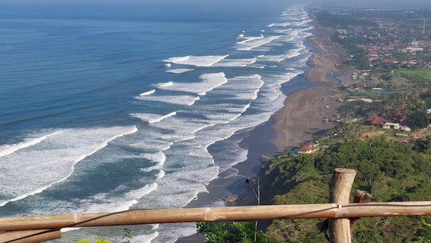 A coastal view with waves, a beach, and a town in the distance. - Bukit Shoka Top View Camp (Giricahyo)