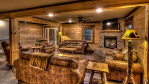 A log cabin interior with a fireplace, leather furniture, and a stone fireplace surround.