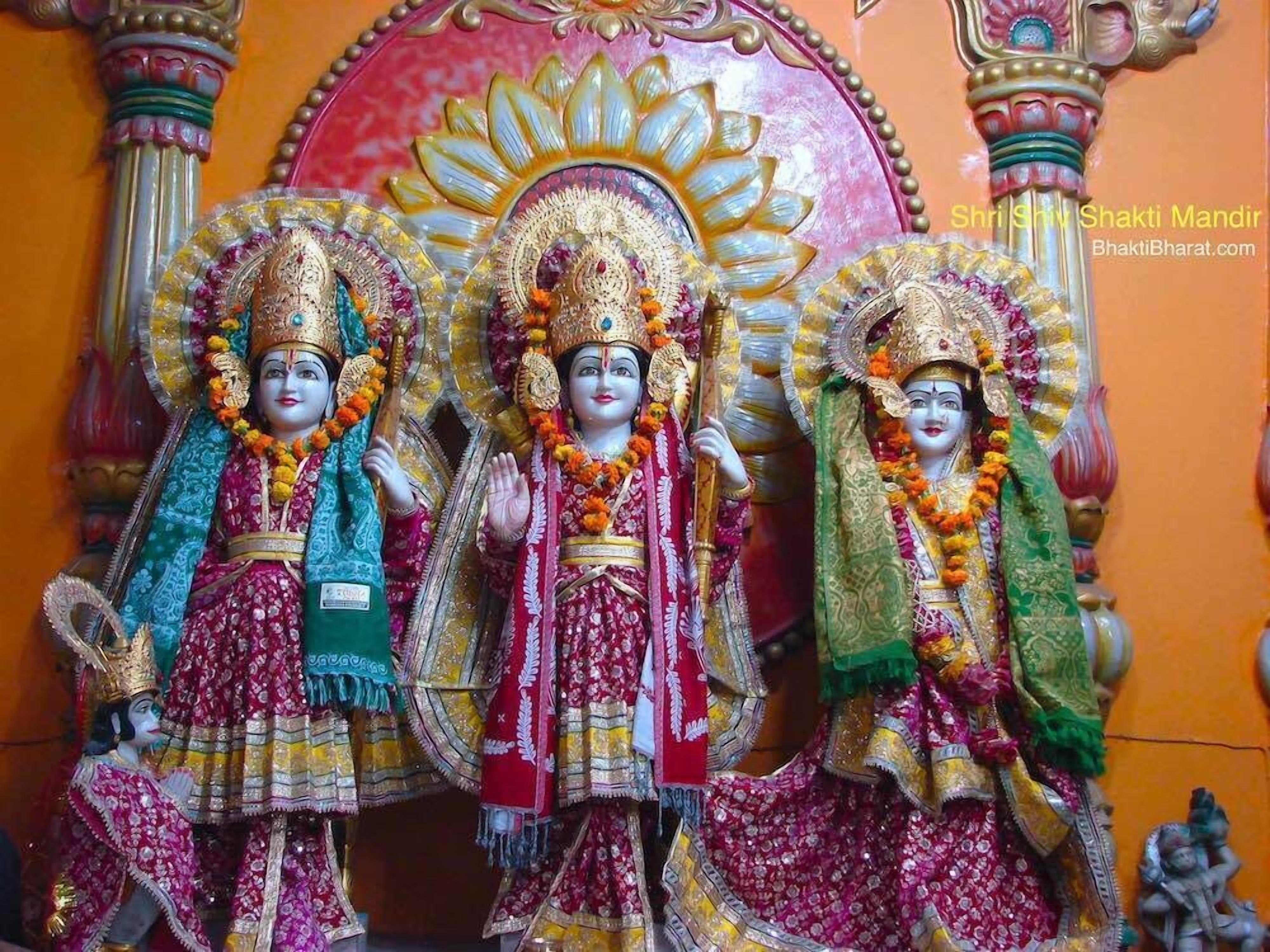 Three statues of deities adorned in traditional attire, set against a backdrop with ornate pillars and a floral design.