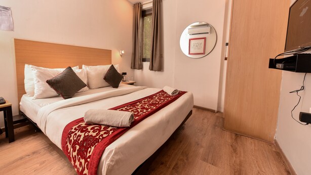 Een hotelkamer met een bed, een houten hoofdbord, een nachtkastje, een spiegel en een houten deur.