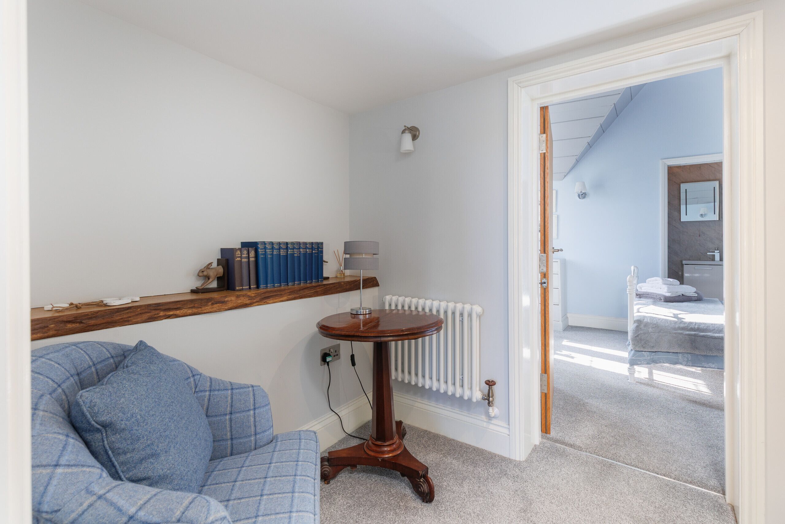 A room with a blue sofa, a wooden side table with books, a white radiator, and a door leading to another room.