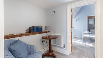 A room with a blue sofa, a wooden side table with books, a white radiator, and a door leading to another room.