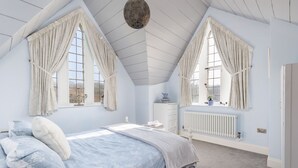 Una camera da letto con soffitto spiovente, un letto con copripiumino a fiori blu, due finestre con tende, una cassettiera bianca e un termosifone.