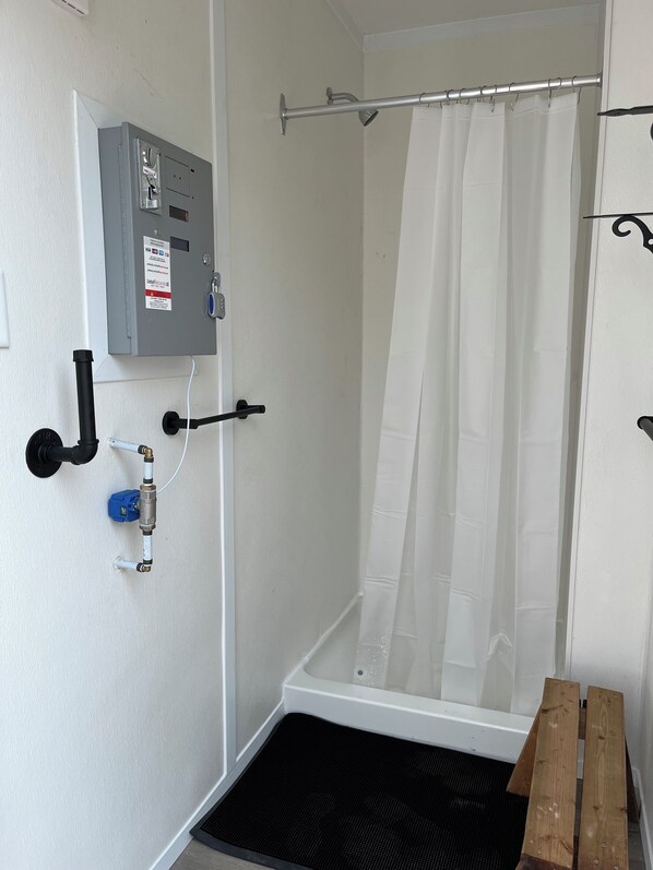 A shower area with a glass door, a shower curtain, a control panel, and a wooden bench.