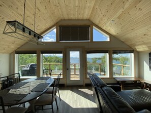 A spacious room with a high ceiling, large windows, a dining area, and a seating area with a view of the outdoors.