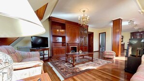 Un salón espacioso con suelo de madera, chimenea, televisor y araña.