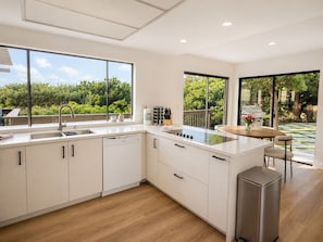 A modern kitchen with large windows, a dishwasher, a gas stove, and a trash bin.