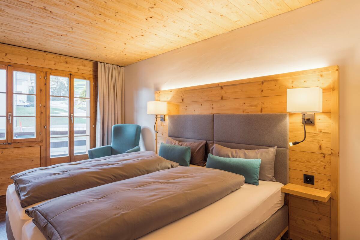 Ein Hotelzimmer mit Holzbalkendecke, einem großen Bett mit vielen Kissen, einem Sessel und einem Nachttisch mit Lampe.