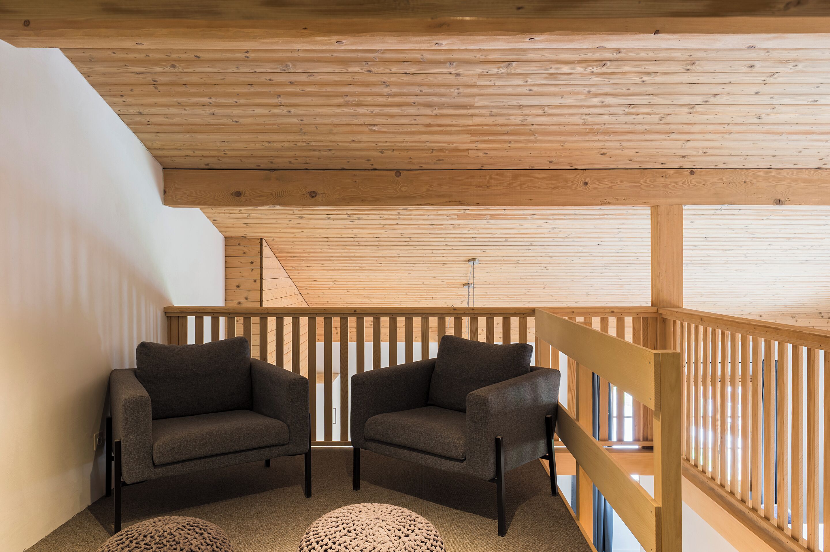 A wooden ceiling with a sloped design, two grey sofas with black legs, and a wooden railing.