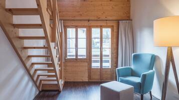 Ein Zimmer mit einer Holztreppe, einem blauen Sessel, einer Stehlampe und einem Fenster mit Vorhängen.
