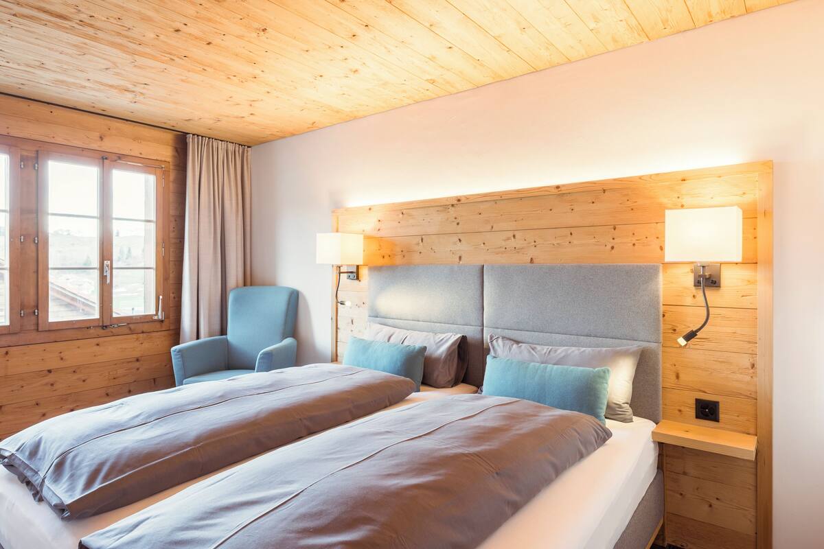 Ein Schlafzimmer mit zwei Betten, Holzboden und einem Fenster mit Vorhängen.