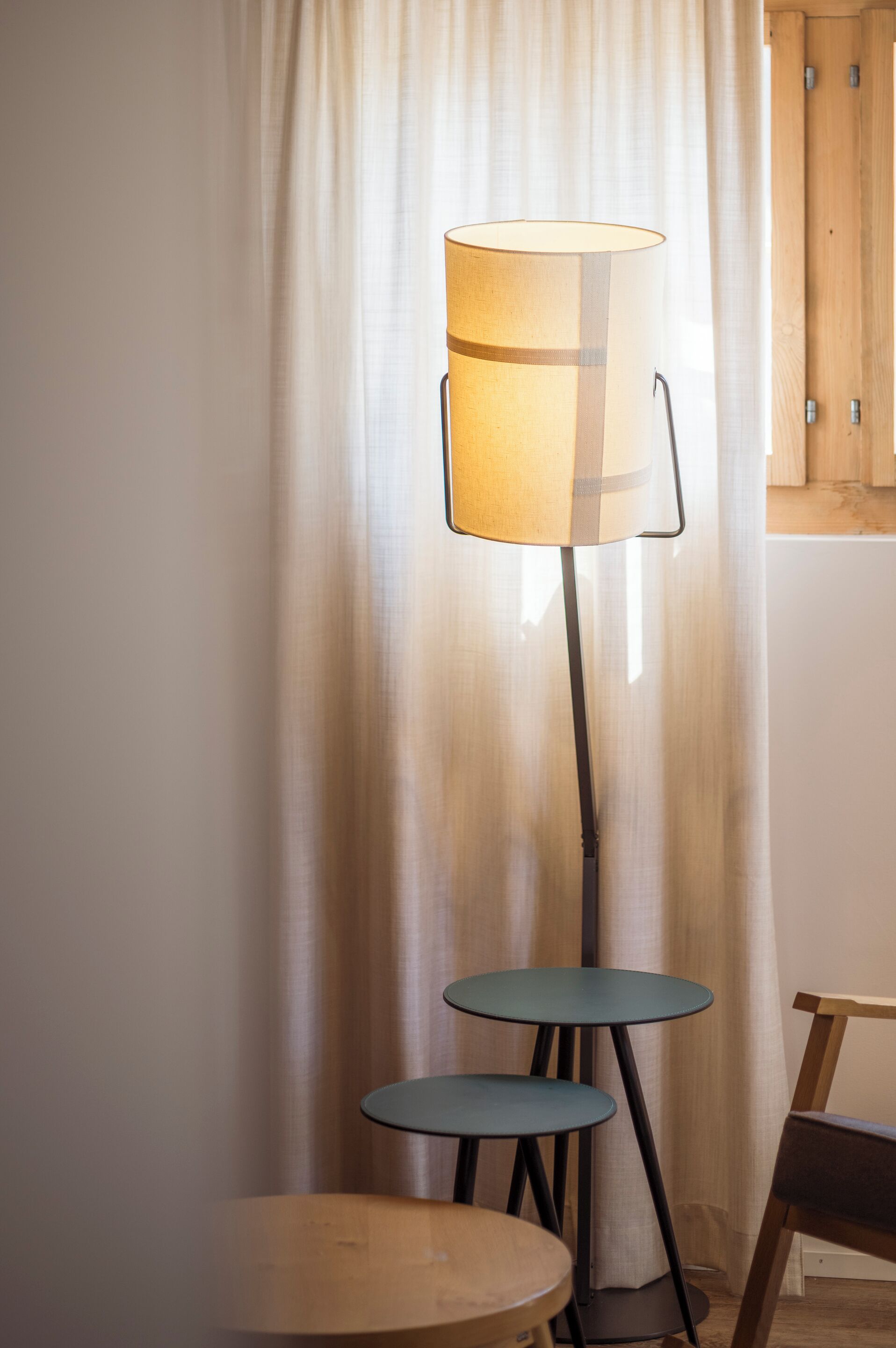 Eine Stehlampe mit zylindrischem Lampenschirm, zwei kleine runde Tische und ein Holzsessel.