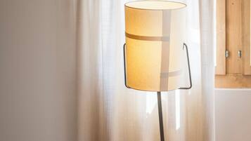 Eine Stehlampe mit zylindrischem Lampenschirm, zwei kleine runde Tische und ein Holzsessel.