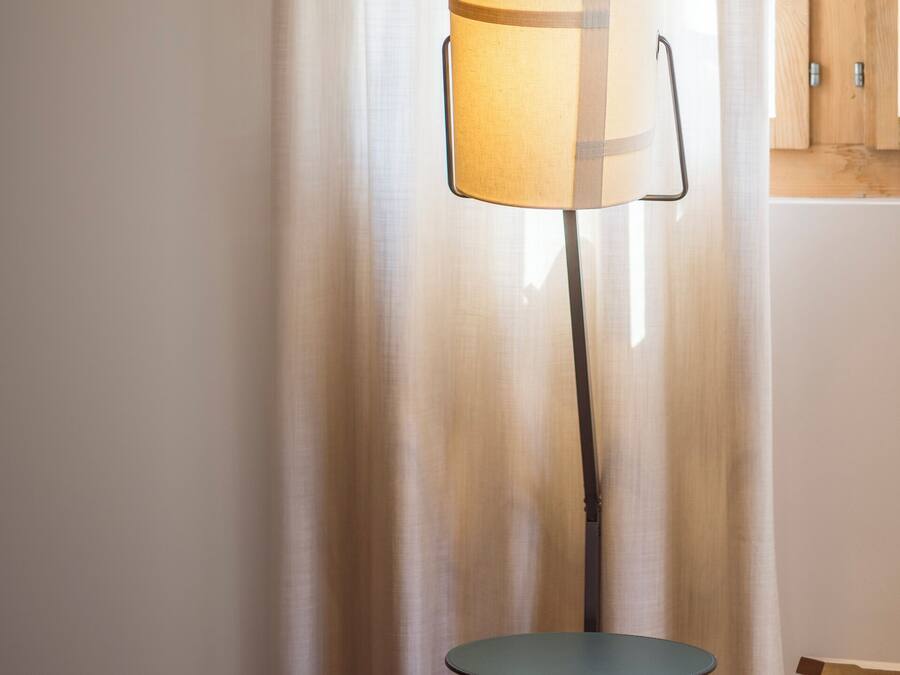 Eine Stehlampe mit zylindrischem Lampenschirm, zwei kleine runde Tische und ein Holzsessel.