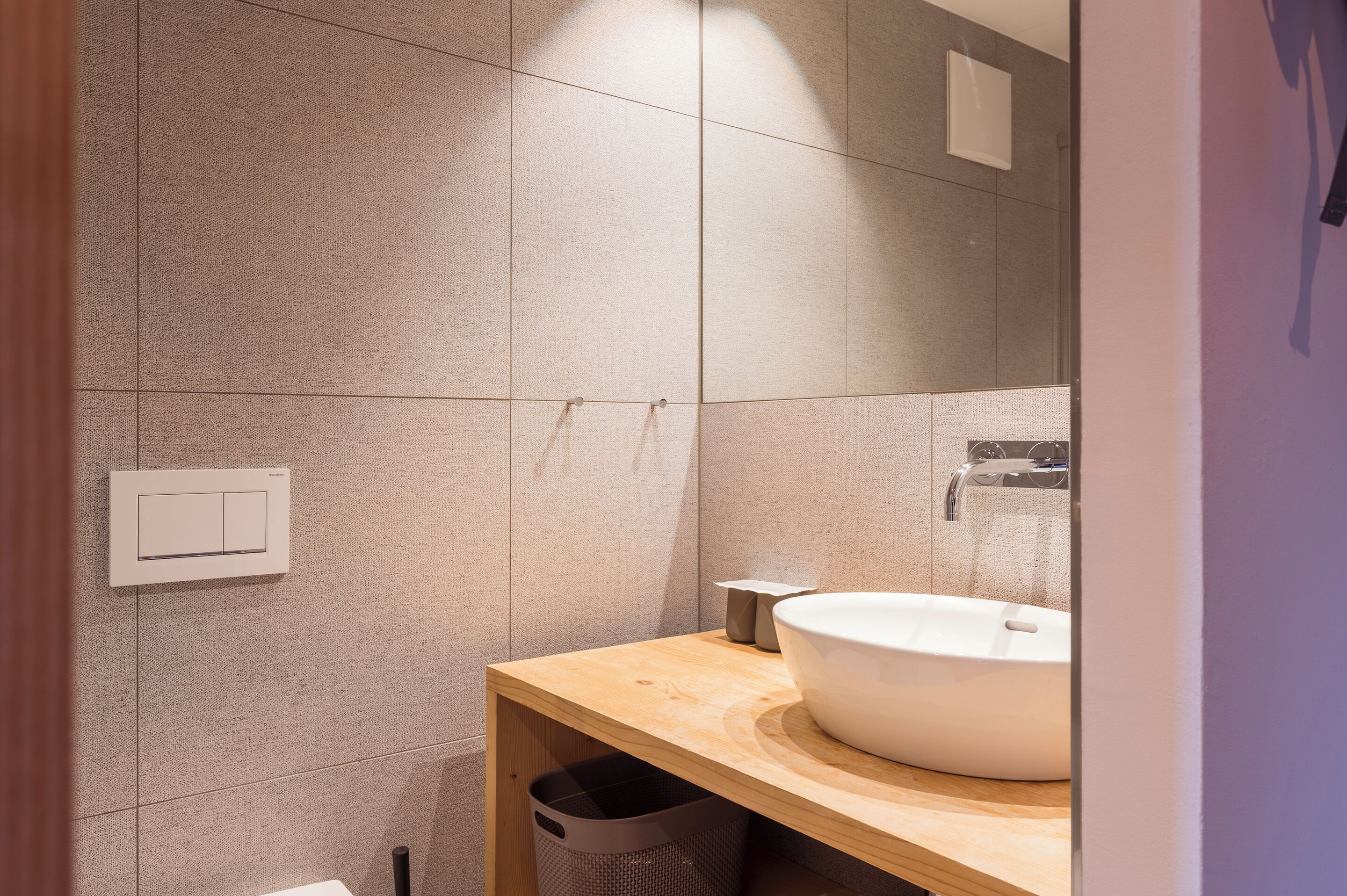 A modern bathroom with a large mirror, a white sink, and a wooden vanity.
