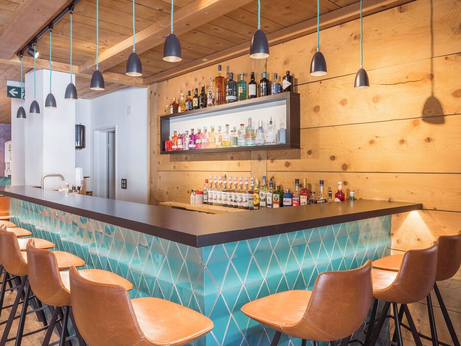 Een bar met een lange toonbank, meerdere hangende lampen en een plank vol verschillende flessen.