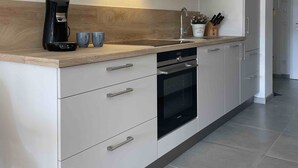 A modern kitchen with white cabinetry, a built-in oven, a coffee maker, and a microwave. - Bergzeit Füssen - Holiday apartment (Füssen)