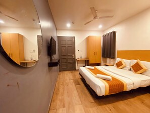 A hotel room with a bed, a TV, a ceiling fan, and a mirror. - Hotel White Saffron (New Delhi)