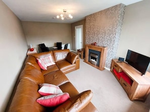 A living room with a brown leather sofa, a fireplace, a television on a wooden stand, and patterned wallpaper.