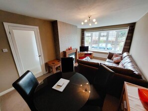 A living room with a sofa, a coffee table, and a TV. There is a window with a view of the outside.