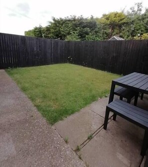 A backyard with a wooden fence, a grassy lawn, and a concrete patio with a table and chairs. - 2 Spring Gardens - 2 bed holiday bungalow (Cayton)