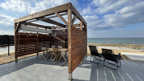 A wooden pergola with a table and chairs, overlooking a beach. - EIGHT POINT RESORT AWAJISHIMA - Glamping (Awaji)