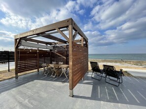 Eine hölzerne Pergola mit Tisch und Stühlen, mit Blick auf einen Strand.