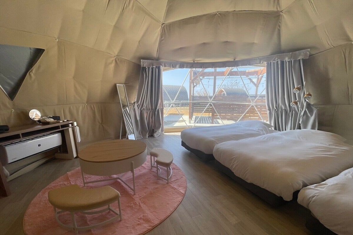 A tent-style room with a bed, a desk, a chair, and a small table.