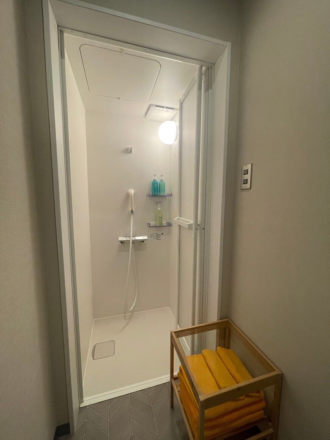 A modern bathroom with a glass-enclosed shower, a wooden bench, and a small shelf with toiletries.
