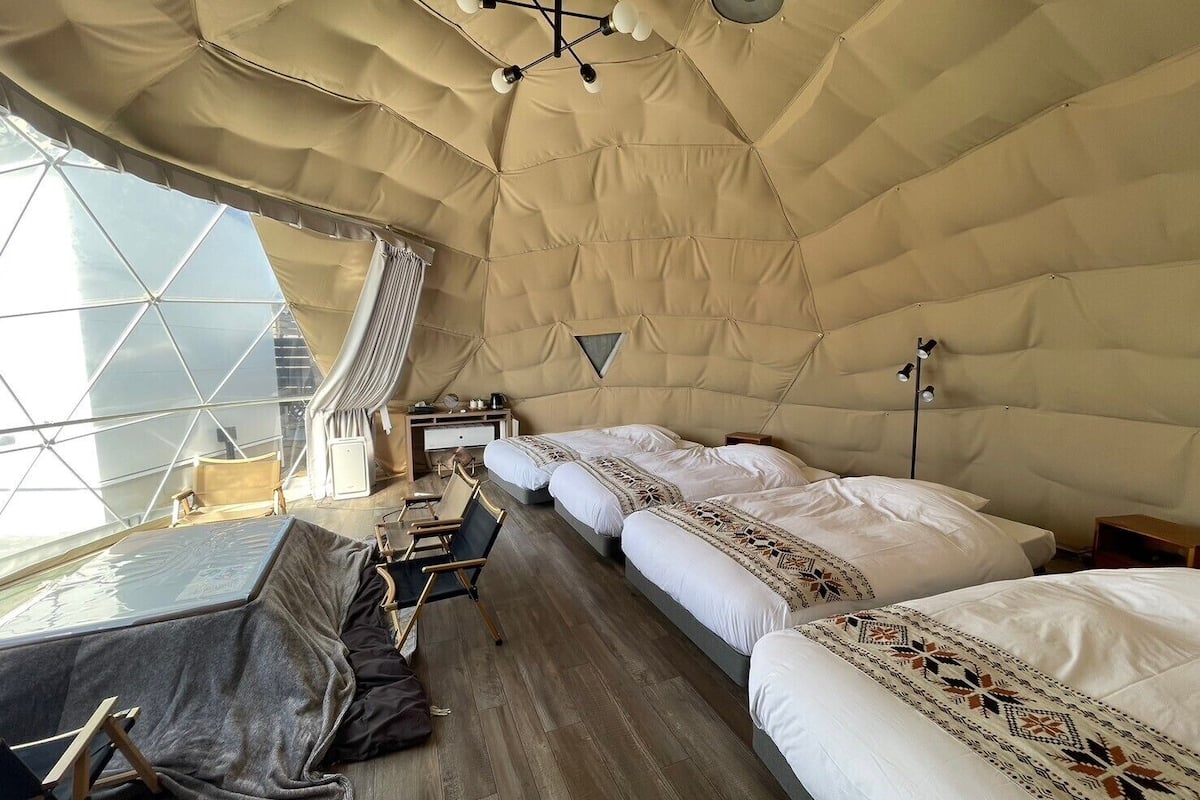 A spacious tent-style room with two beds, a desk, and a chair.