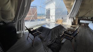 A modern, spacious room with a large window offering a view of the cityscape. The room features a central table with chairs, a small seating area, and a kitchenette. - EIGHT POINT RESORT AWAJISHIMA - Glamping (Awaji)