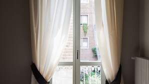 Une pièce avec une fenêtre ornée de rideaux blancs, donnant sur un bâtiment en briques, et un radiateur blanc.