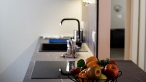Une cuisine équipée d’un évier et d’un panier de fruits contenant des pommes, des oranges et une fraise.
