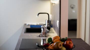 A kitchen with a sink and a fruit bowl containing apples, oranges, and a strawberry.