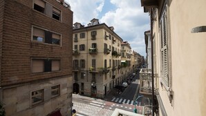 Une rue étroite, bordée de bâtiments des deux côtés, avec des balcons ornés de plantes et un passage piéton.