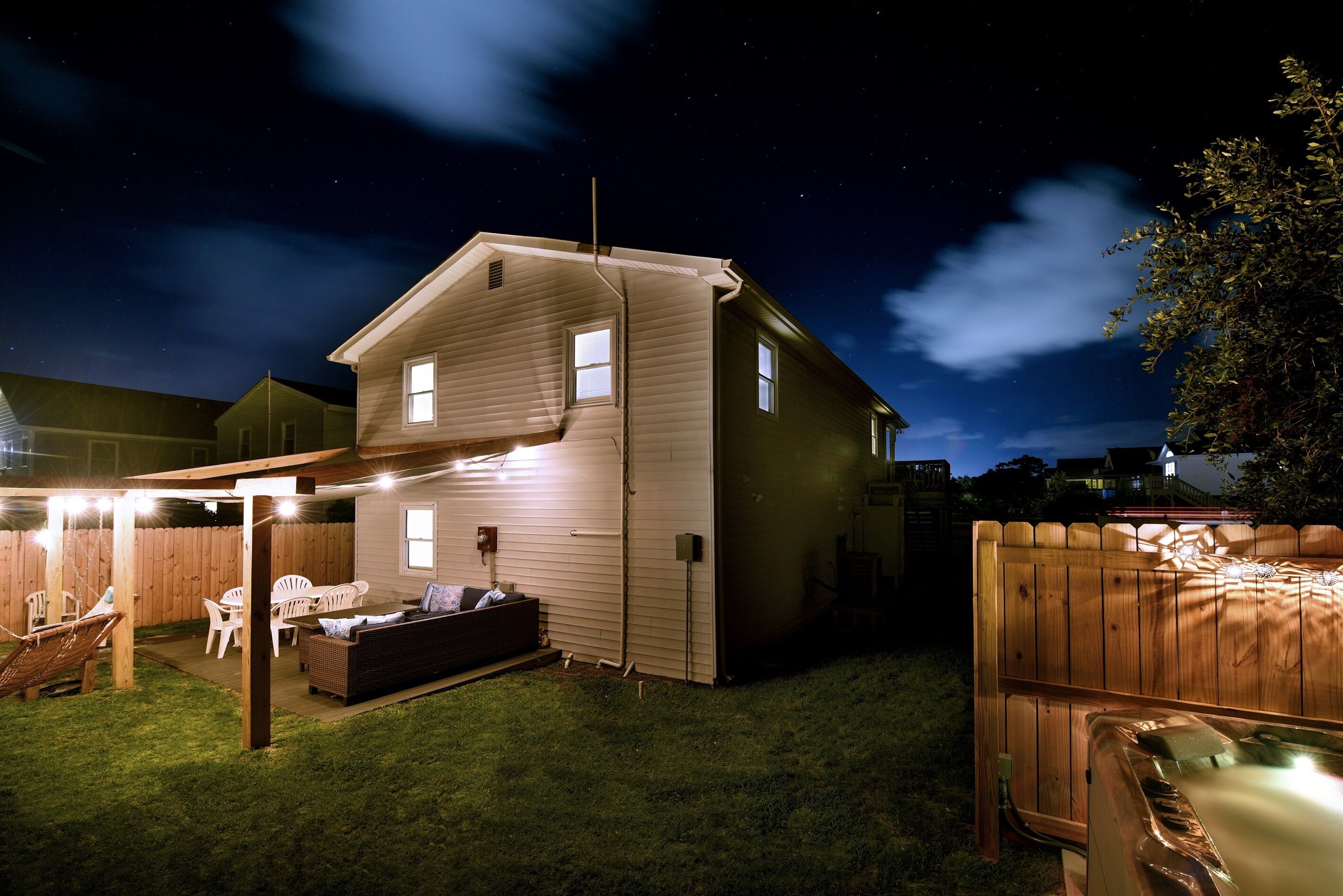 Ein zweistöckiges Haus mit überdachter Terrasse, Whirlpool und einem umzäunten Garten.