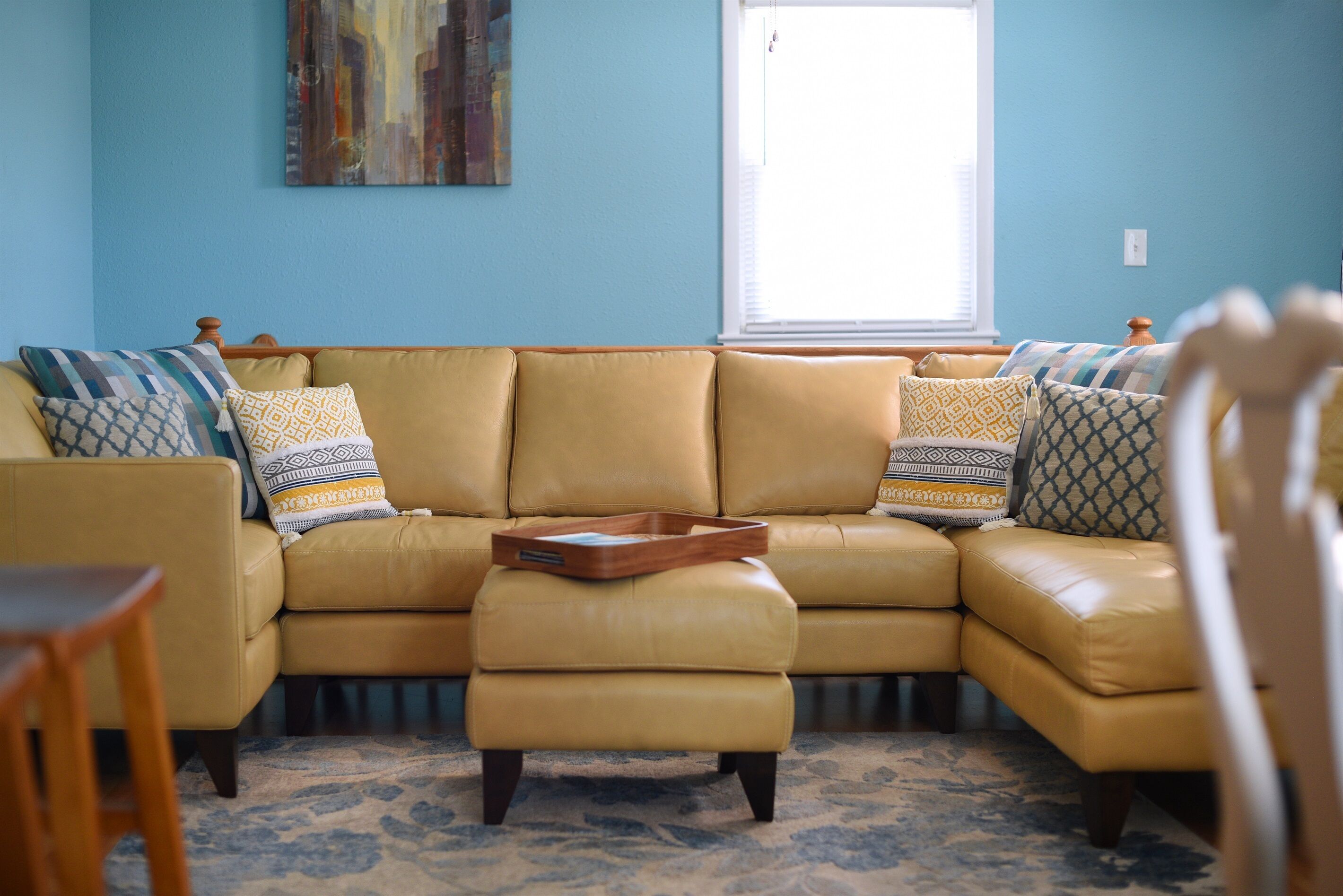 Ein Wohnzimmer mit einem sandfarbenen Ledersofa, gemusterten Kissen, einem Holztisch und einem blauen Teppich.