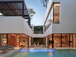 A modern house with a swimming pool, large glass windows, and a well-lit interior. - Villa Nini Elly (Canggu)
